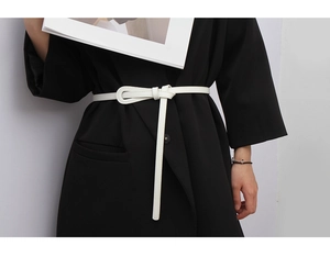 Minimalist white leather skinny belt featuring a stylish knot buckle detail on a black blazer