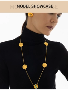 Detail der goldenen Wabenhalskette mit grünen Steinen und Blumenohrring auf schwarzem Pullover