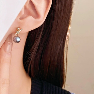 Close-up of gold stud earring with grey pearl and zircon bow detail on model's ear