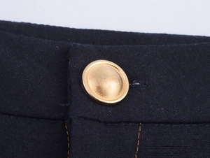Macro shot of circular golden metal button with textured finish on dark navy fabric