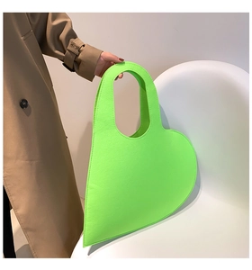 Detail of neon green heart-shaped felt handbag held by a model in a trench coat
