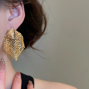 Macro detail of geometric mesh earrings with warm gold finish on a model side view