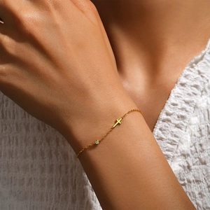 Close-up of gold minimalist cross bracelet with single round diamond on wrist