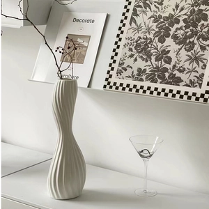 Detail of a white twisted ceramic vase with a wave design on a minimalist white shelf
