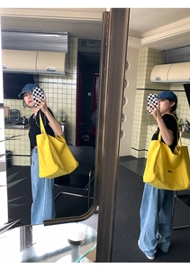 Close-up of yellow large canvas tote bag with front pocket shown on shoulder