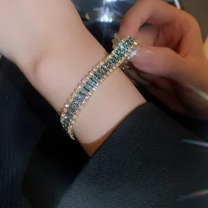 Elegant triple-row blue and white crystal tennis bracelet worn on wrist over dark suit
