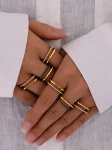 Detail of stacked gold cubic zirconia rings featuring white and green crystals on hand