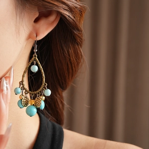 Close-up of vintage bronze bamboo waterdrop earrings with blue beads worn on model