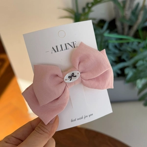 Detailed close-up of a pink cotton bow hair clip featuring a white central emblem on display