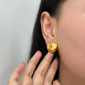 Close-up of a large irregular gold geometric earring worn on a model's ear