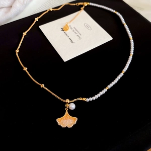 Detail of gold ginkgo leaf necklace with zircon and white pearl on a gift card