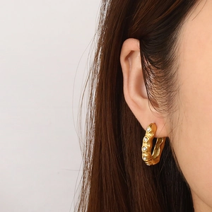 Detail of gold U-shaped earring with irregular texture and sparkling zircon inlay