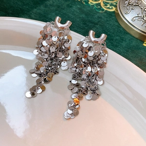 Close-up of silver U-shaped sequin tassel earrings on a vintage porcelain plate