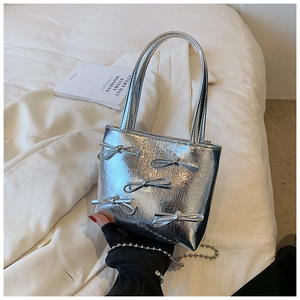 Detail view of silver metallic tote bag with decorative bows and shiny wrinkled texture