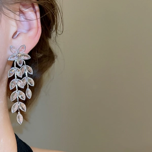 Detailed view of silver flower and leaf drop earrings with sparkling crystals on model