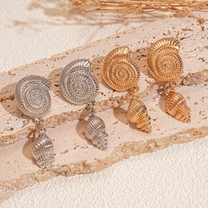 Golden and silver spiral conch shell drop earrings on a natural beige stone surface