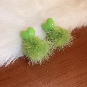Detailed view of green heart-shaped stud earrings with fluffy fur ball drop ornaments