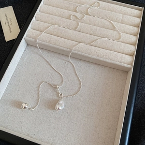 Detail view of a silver bead and irregular pearl pendant on a sleek chain necklace