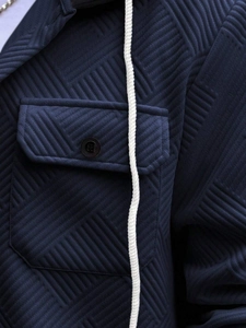 Detail of navy blue hoodie featuring geometric textured fabric and buttoned chest pocket
