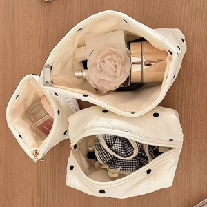 Détail de trois trousses de maquillage matelassées à pois sur une table en bois