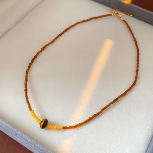 Detailed shot of amber beaded necklace with yellow accents and a tiger eye stone pendant