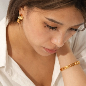 Detail of 18K gold-plated flower earrings and bracelet with pearls on a model