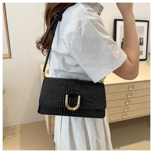 Detail of black crocodile pattern leather handbag with gold U-shaped metal buckle and knot strap