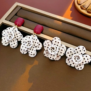 Détail de boucles d'oreilles fleur à pois noirs et accent carré rouge sur un plateau