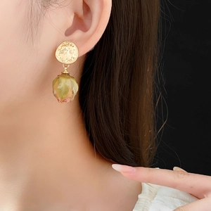 Close-up of golden hammered earrings featuring a resin-preserved rose bud pendant