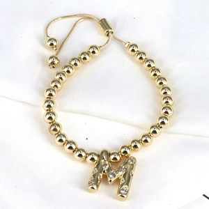 Detailed close-up of a golden beaded bracelet with a zircon-inlaid letter M pendant
