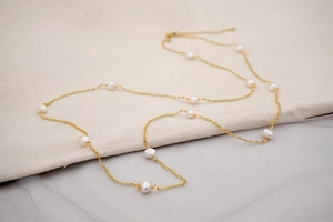 Detail of long gold chain necklace featuring spaced baroque freshwater pearls for layering