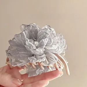 Detail einer grauen Haarklammer mit Netzblume und Perle in der Hand gehalten