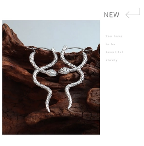 Macro shot of silver snake hoop earrings with scale texture on a dark wood background