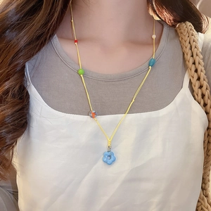 Detail of beaded flower necklace with blue pendant and colorful stones on yellow cord