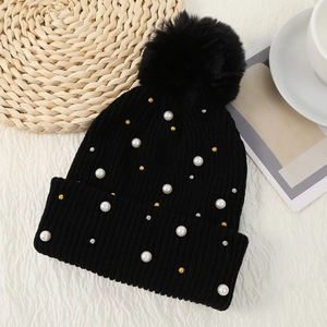 Detail of black knit beanie with faux fur pompom and pearl accents on cozy background