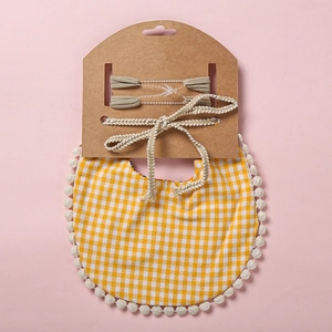 Détail d'un bavoir bébé à carreaux jaunes avec pompons et deux bandeaux dorés assortis