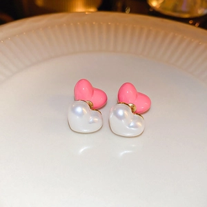 Détail de boucles d'oreilles double cœur rose et perle sur un plat en céramique blanc