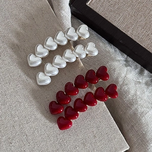 Elegant curved heart hair clips in pearl white and deep red on a textured linen background