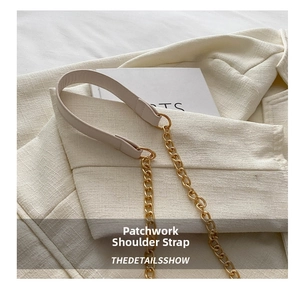 Detail shot of a beige leather shoulder strap with a chunky gold chain on tweed fabric