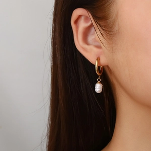 Golden stainless steel hoop earrings with freshwater pearl charms shown on a female model