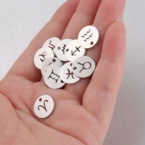 Macro shot of 12mm stainless steel zodiac pendants with cutout signs on palm