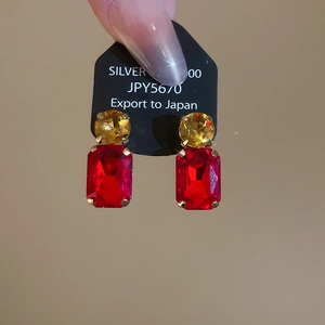 Detailed shot of gold earrings with round yellow and rectangular red gems on display card