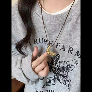 Primo piano di una collana con ciondolo a croissant dorato e cordino nero su una modella.