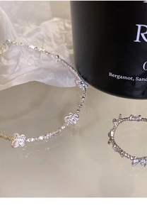 Dettaglio della collana a farfalla in argento S925 e set di anelli su piano riflettente