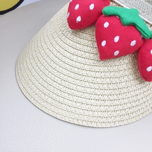 Close-up of woven straw sun hat texture featuring decorative red fabric strawberries