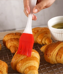 Close-up of a silicone pastry brush applying oil to a croissant on a grill rack