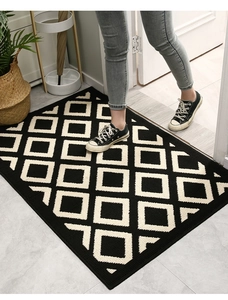 Close-up of feet on black and beige geometric patterned door mat at home entryway