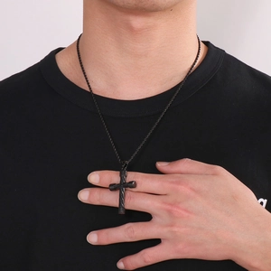 Close-up of black stainless steel cross pendant necklace worn by male model on black t-shirt
