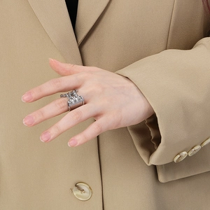 Detail of silver crossover ring with pavé zircons worn on finger with a beige suit