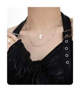 Detail of layered irregular lava pendant necklace and textured silver ring on model
